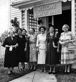 A vintage photo of seven woman standing in a doorway under a "Welcome Women of Brandeis" sign